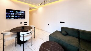 Un soggiorno moderno con una TV a schermo piatto, un tavolo da pranzo rotondo con sedie, un divano e un originale lampadario.