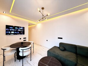 Ein modernes Wohnzimmer mit einem Flachbildfernseher, einem runden Esstisch mit Stühlen, einer Couch und einer außergewöhnlichen Deckenleuchte.