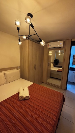 A hotel room with a bed, a wooden wardrobe, a mirror, and a ceiling light fixture. - Bellenus - balcony, hammock, comfort. (João Pessoa)