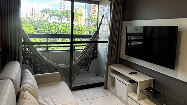 Un salon moderne avec un canapé, un téléviseur et une vue sur la verdure et les bâtiments.