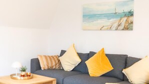 A living room with a grey sofa, yellow and striped pillows, a wooden coffee table with a lamp, and a painting of a beach scene. - Helga's Stadthaus (Nordhorn)