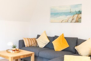 A living room with a grey sofa, yellow and striped pillows, a wooden coffee table with a lamp, and a painting of a beach scene. - Helga's Stadthaus | vacation apartment, business apartment & temporary apartment in Nordhorn - Pets welcome (Nordhorn)