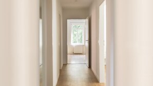 A narrow hallway with a wooden floor leading to a door with a window. - Helga's Stadthaus (Nordhorn)