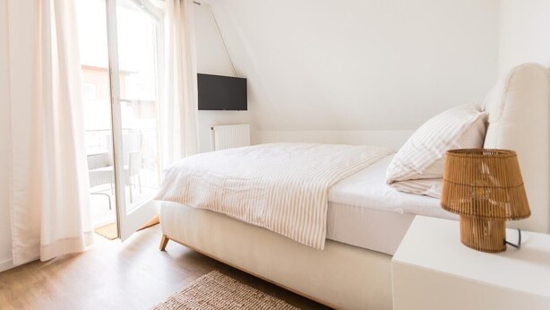 A bedroom with a bed, a TV, a lamp, and a view of the outdoors. - Helga's Stadthaus (Nordhorn)