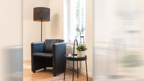 A room with a black leather chair, a floor lamp, a small table with a plant, and a radiator. - Helga's Stadthaus (Nordhorn)