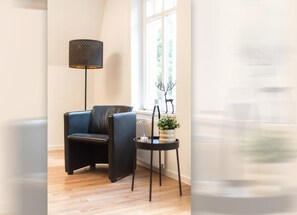 A room with a black leather chair, a floor lamp, a small table with a plant, and a radiator. - Helga's Stadthaus | vacation apartment, business apartment & temporary apartment in Nordhorn - Pets welcome (Nordhorn)