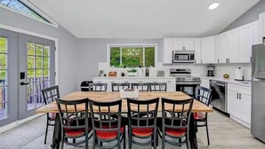 A modern kitchen with white cabinets, a central island, and a dining area with a wooden table and chairs. - Poconos Chalet, Game Room, Hot Tub & Firepit (Tobyhanna)