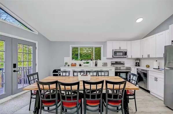 Une cuisine moderne avec des meubles blancs, un îlot central et un coin repas comprenant une table et des chaises en bois.