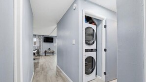 A laundry room with a washing machine and dryer, a television in the background, and a wooden floor. - Poconos Chalet, Game Room, Hot Tub & Firepit (Tobyhanna)