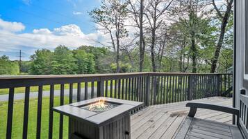 A wooden deck with a fire pit, surrounded by trees and a road.