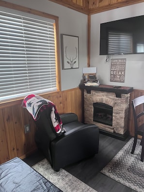 A cozy cabin interior with a fireplace, a mounted television, and a framed deer head artwork.
