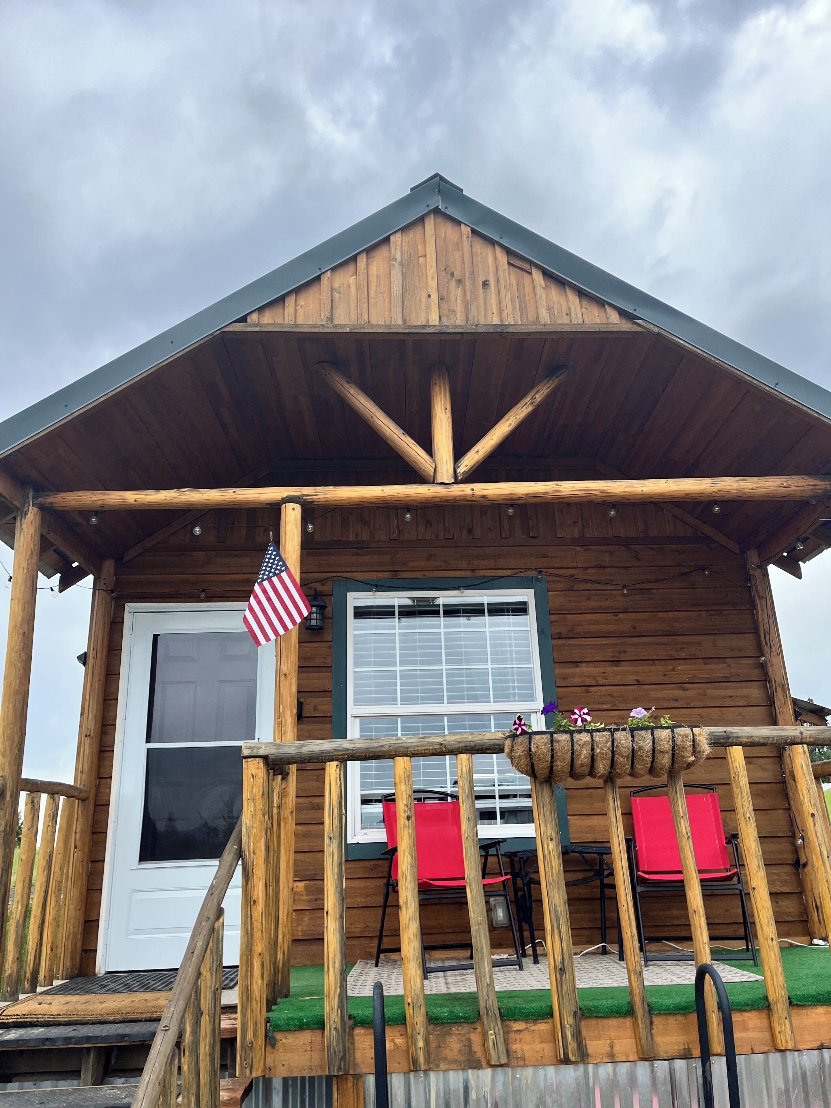 A wooden cabin with a porch, a door with an American flag, and a window.