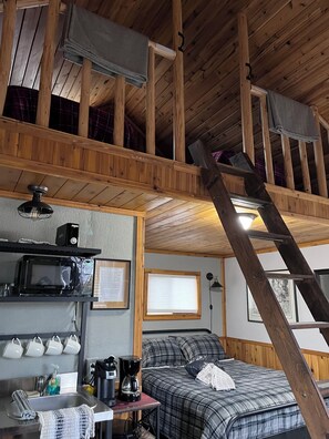 A cabin interior with a loft bed, a kitchen area with a microwave, and a staircase.