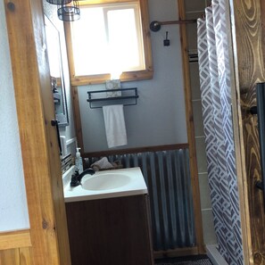 A bathroom with a wooden door, a white sink, a mirror, a towel rack, and a shower curtain.