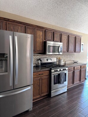 A kitchen with a stainless steel refrigerator, a microwave, a stove, and wooden cabinets. - Private Garden Retreat in Frisco TX - 3 bedroom and 2 full baths (Frisco)