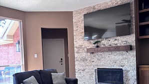 Un salon avec un mur en pierre, une cheminée, un ventilateur de plafond et un grand téléviseur.