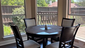 Un coin repas comprenant une table ronde, quatre chaises, un lustre et de grandes fenêtres donnant sur un jardin.