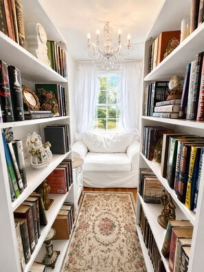 Un coin lecture accueillant avec un canapé blanc, des étagères remplies de livres, une horloge décorative et un lustre.