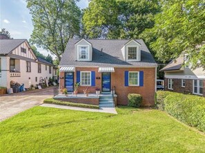Une maison à deux étages avec un porche à l’avant, un petit jardin et une allée.