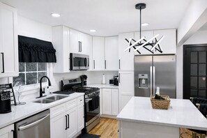 Une cuisine moderne avec des meubles blancs, des appareils en acier inoxydable, un coin café et un élément décoratif mural.