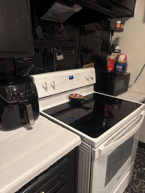 Une cuisine avec un four blanc, une plaque de cuisson à induction noire, une machine à café PowerXL et un four à micro-ondes.