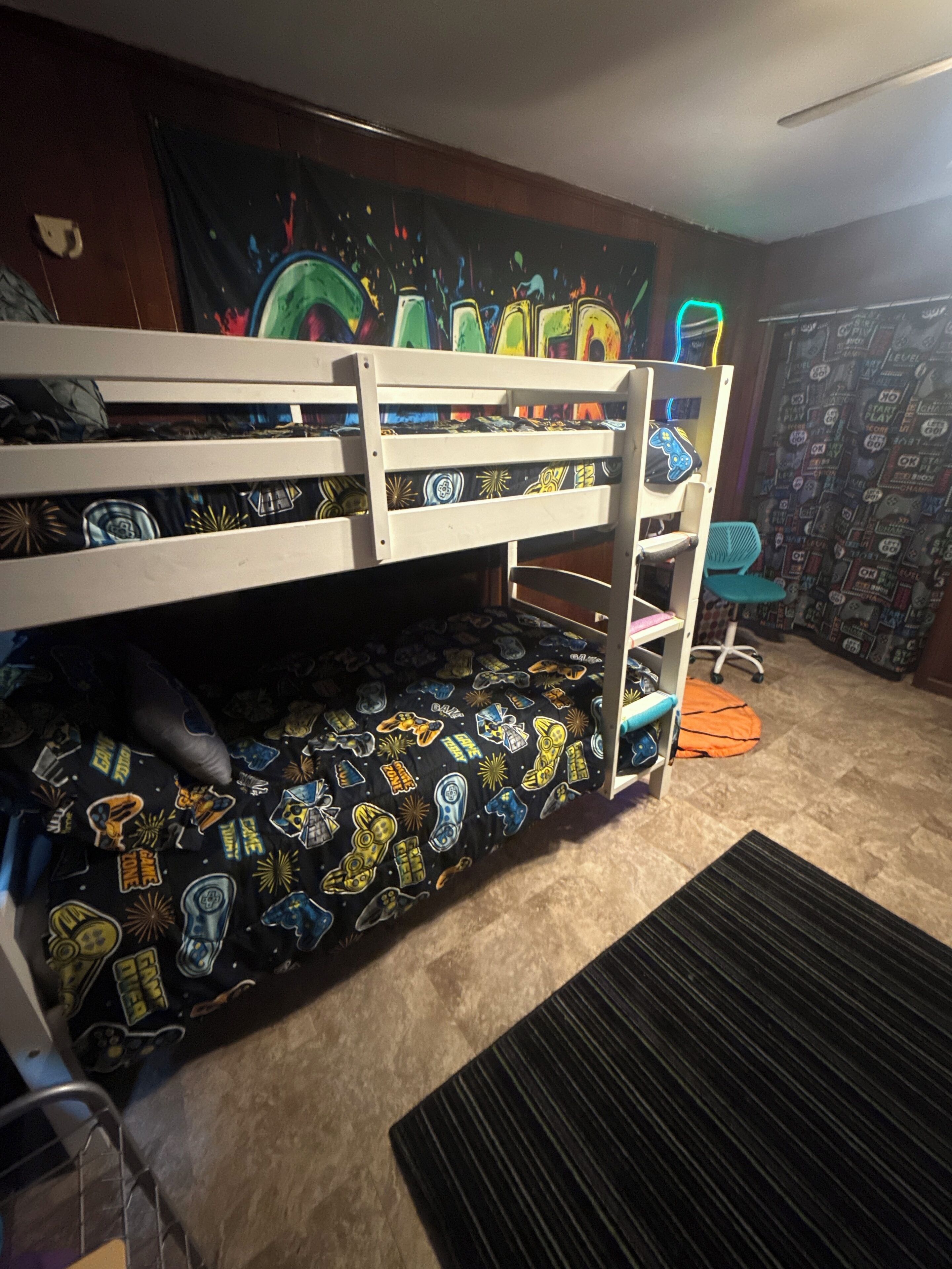 A bunk bed with a space-themed bedspread, a blue chair, and a wall with a pattern.