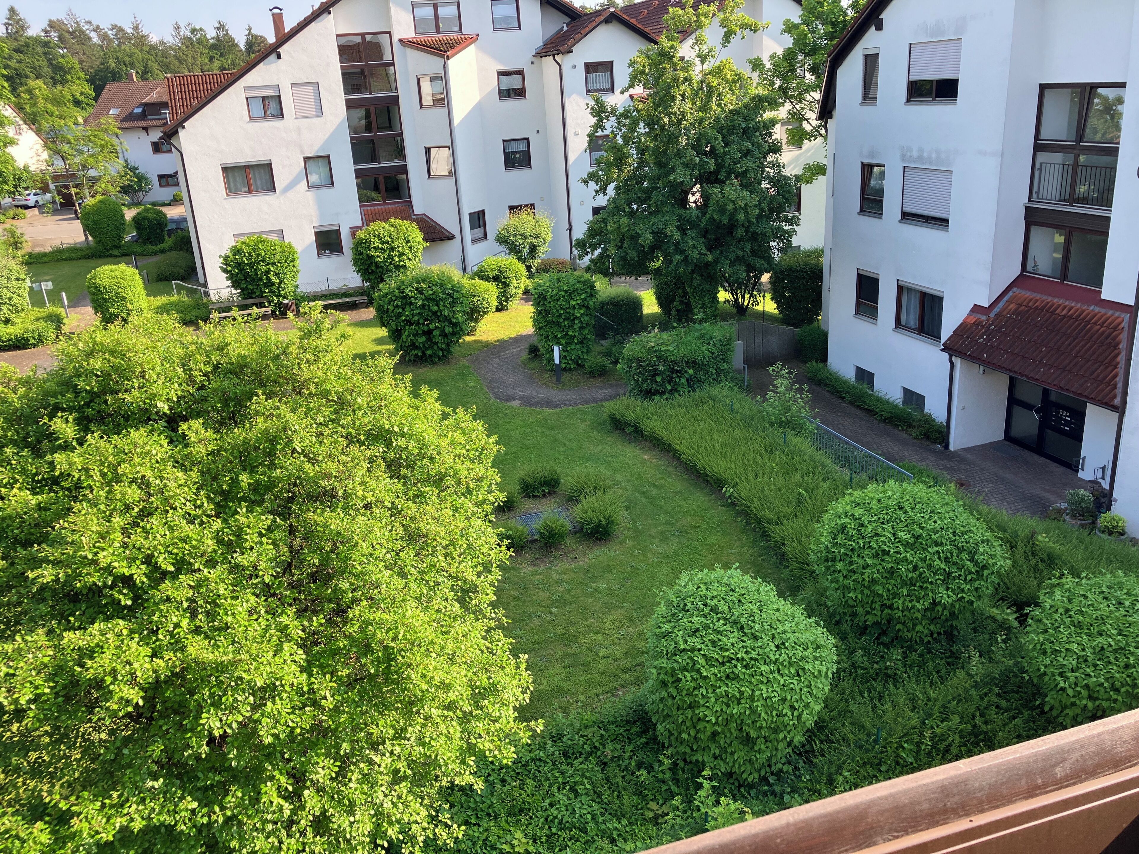 Un immeuble résidentiel doté de nombreux balcons, d’un jardin bien entretenu avec divers arbustes et arbres, et d’une allée pavée.