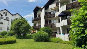 Um edifício residencial com vários andares, varandas, um jardim bem cuidado e um céu azul claro.