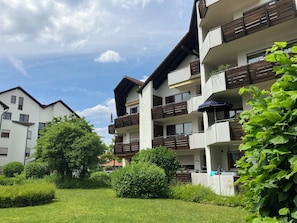 Ein mehrstöckiges Wohngebäude mit Balkonen, einem gepflegten Garten und blauem Himmel.