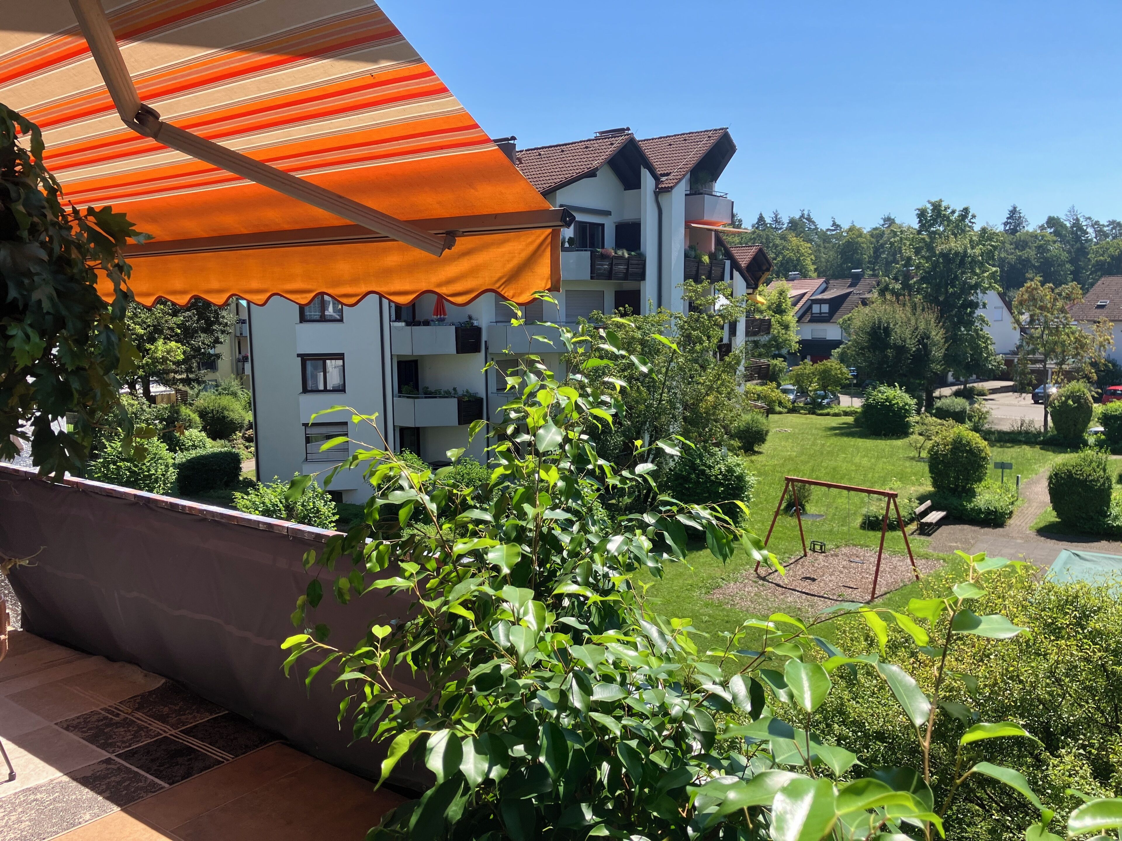Un immeuble résidentiel doté de nombreux balcons, d’un jardin avec une balançoire et d’un auvent à rayures.