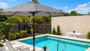 A swimming pool with a tiled deck, white lounge chairs, a striped umbrella, and a small table with a plant. - Boutique apartment with ocean view, pool, 2 blocks from the beach! (Rincón de Guayabitos)