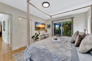 A bedroom with a large bed, a desk, a globe, and a painting.