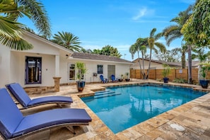 A swimming pool with lounge chairs, a small house, and palm trees.