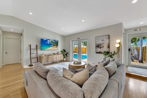 A living room with a large sofa, a TV, a wooden cabinet, and a pool view.