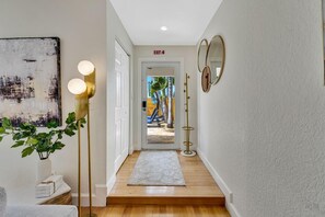 Un couloir avec une porte blanche, un porte-manteau, une lampe sur pied, un tapis et un tableau accroché au mur.
