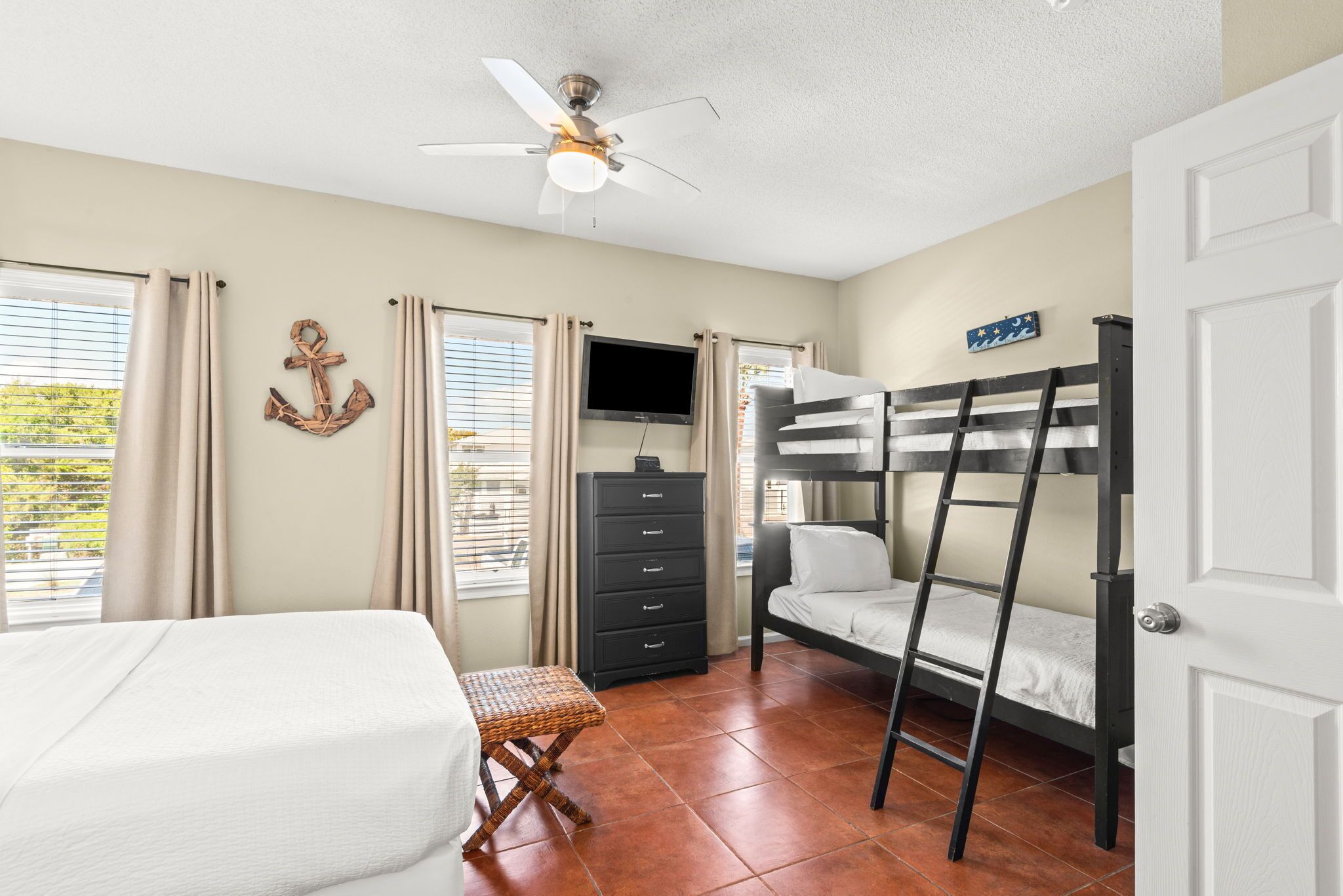 A bedroom with a bunk bed, a desk, a television, a dresser, and a ceiling fan.