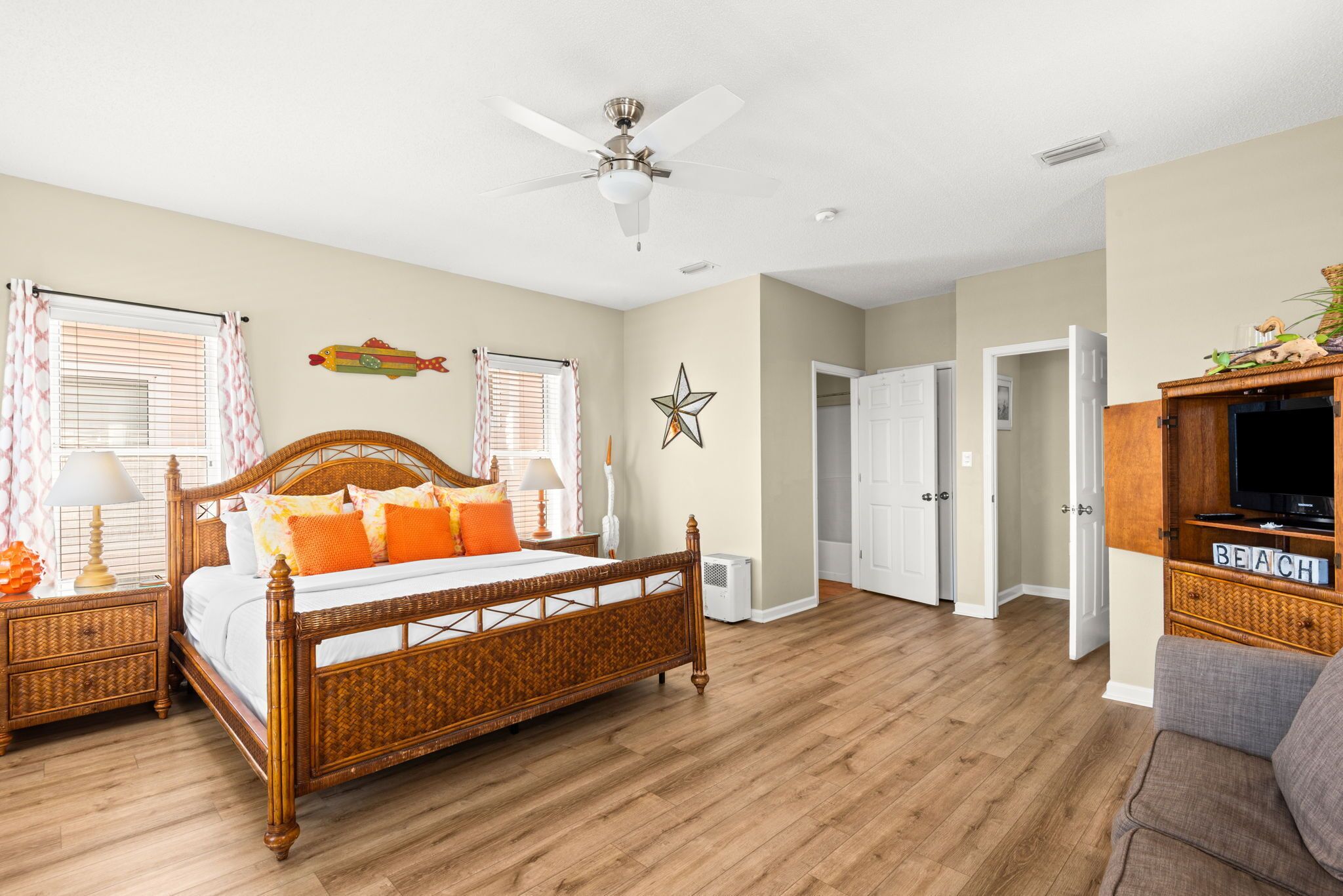 A bedroom with a wooden bed, a ceiling fan, a television, and a sign that says 'BEACH'.