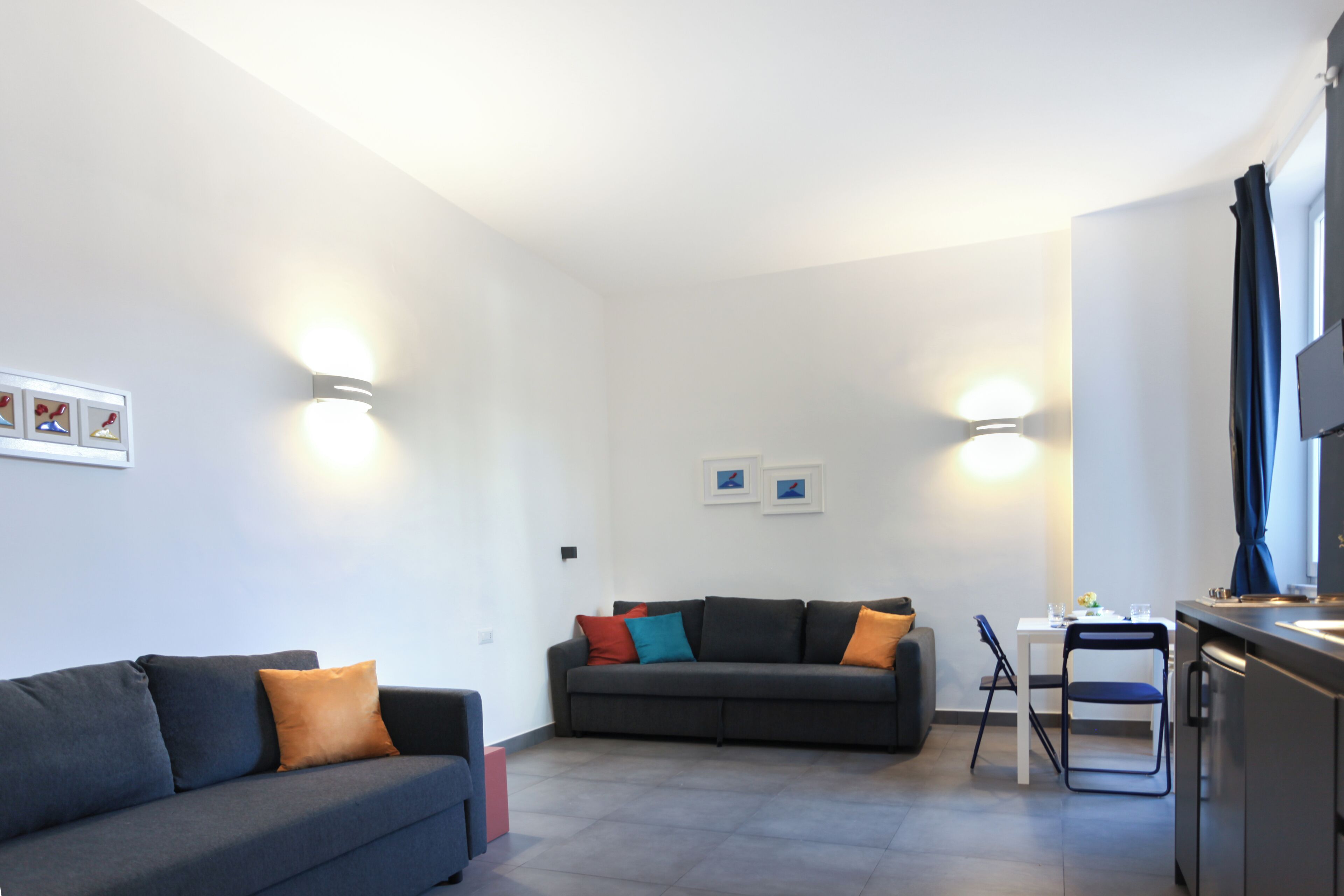A modern living room with a sofa and a dining table, a kitchen area with a counter and cabinets, and a small seating area with a chair.