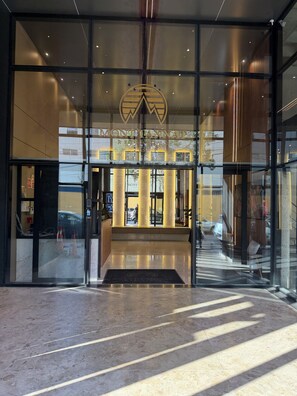 Ein moderner Hotel Eingang mit Glastüren, einem zentralen Empfangsbereich und einer sichtbaren Treppe zum Innenbereich.