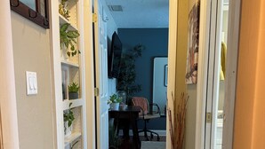 A hallway with a door leading to a room, a wall-mounted TV, and a plant shelf. - Comfort in the Cape (Cape Coral)