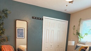 A bedroom with a bed, a desk, a chair, a mirror, a wardrobe, and a window with blinds. - Comfort in the Cape (Cape Coral)