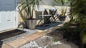 A house with a white door, a window, a potted plant, a folding chair, and a doormat. - Comfort in the Cape (Cape Coral)