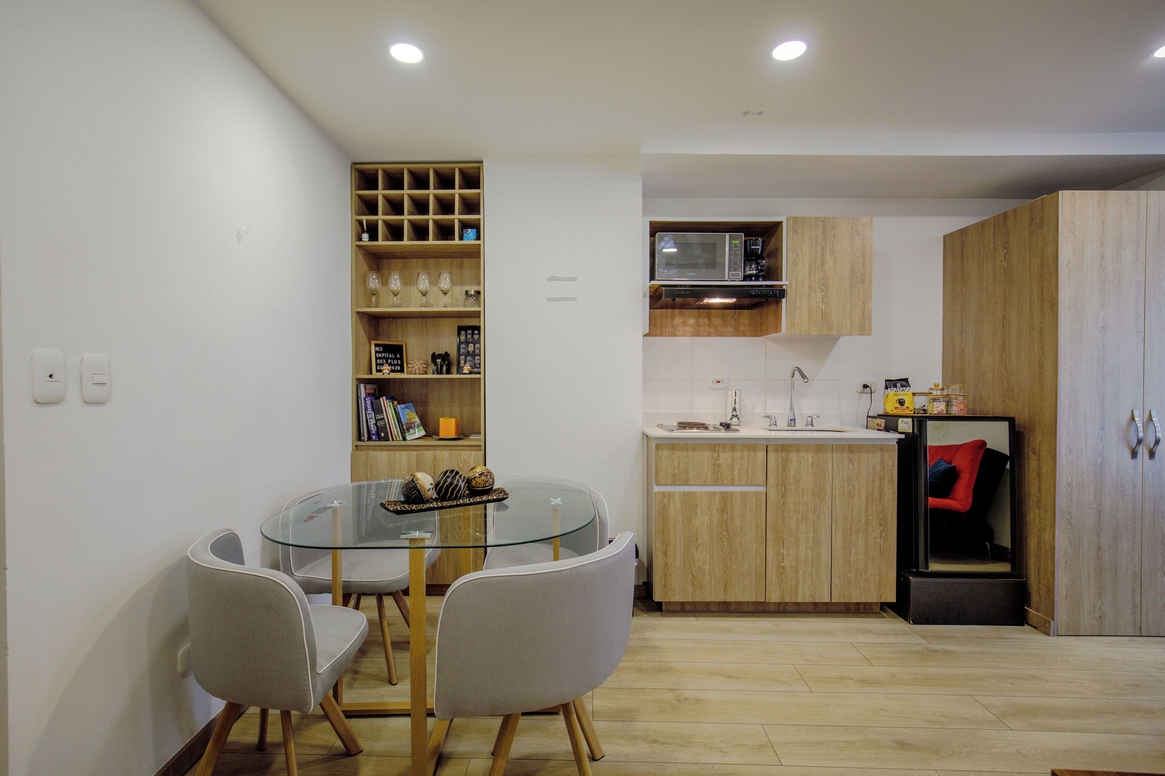 A compact kitchen with a glass dining table, wooden cabinets, and a microwave.