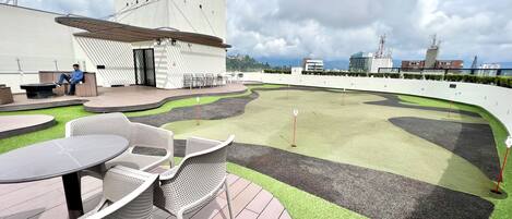 A rooftop terrace with outdoor seating, a small building, and a view of the city skyline.