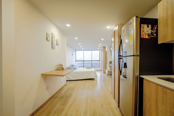 A modern kitchen with a refrigerator, wooden cabinets, and a window providing a view. - Hostara Edificio Capitalia (Manizales)