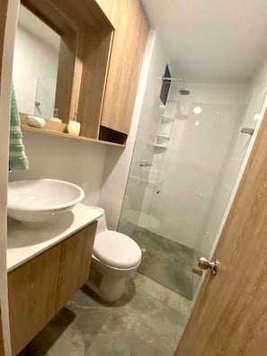 A bathroom with a toilet, a sink, a mirror, and a shower enclosure. - Hostara Edificio Capitalia (Manizales)