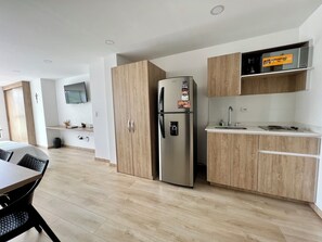 A modern kitchen with wooden cabinets, a stainless steel refrigerator, a microwave, and a sink. - Hostara Edificio Capitalia (Manizales)