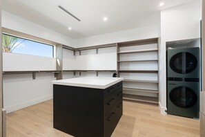 Ein moderner Waschraum mit eingebauten Waschmaschinen und Trocknern, einer großen Insel mit Schubladen und einem Fenster für natürliches Licht.