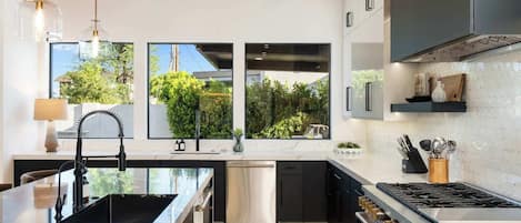 A modern kitchen with a central island, stainless steel appliances, and large windows offering a view of greenery.