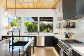 A modern kitchen with a central island, stainless steel appliances, and large windows offering a view of greenery.